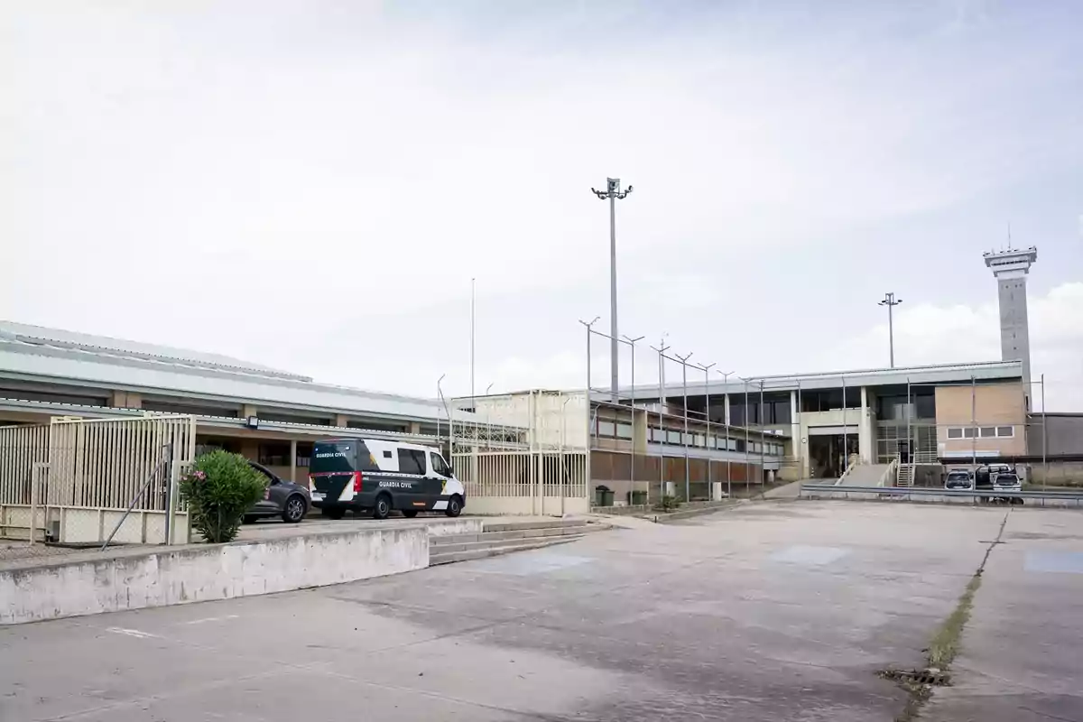 Edificio de una prisión con una furgoneta de la Guardia Civil estacionada en la entrada y una torre de vigilancia al fondo Edificio de una prisión con una furgoneta de la Guardia Civil estacionada en la entrada y una torre de vigilancia al fondo