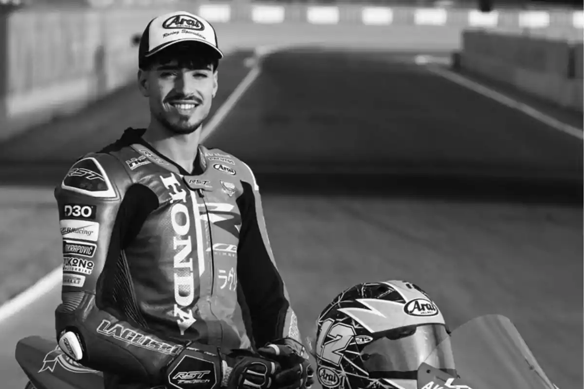 Piloto de motociclismo sonriente con traje de carreras Honda y casco sobre una motocicleta en un circuito
