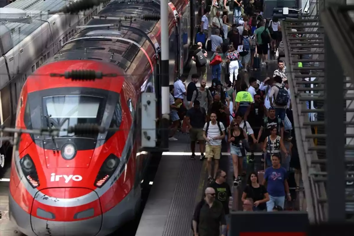 Tren rojo de alta velocidad en una estación concurrida con muchas personas caminando por el andén Tren rojo de alta velocidad en una estación concurrida con muchas personas caminando por el andén