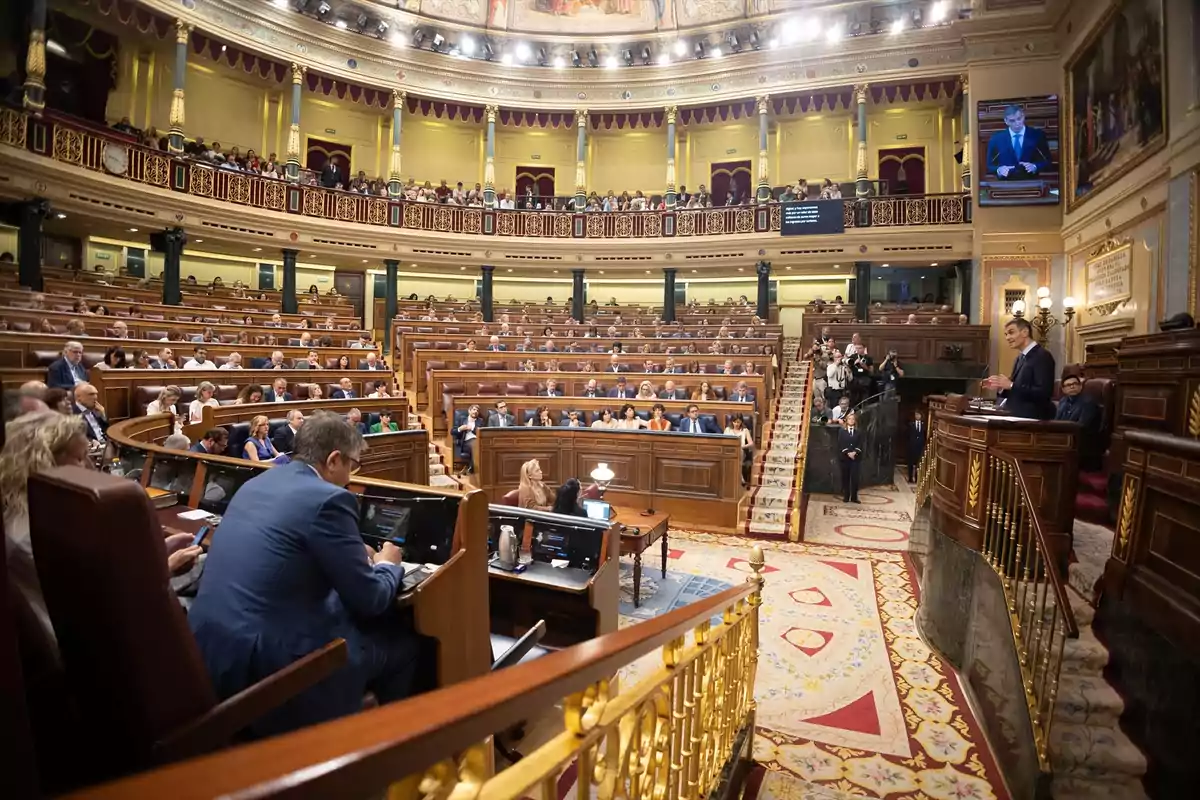 Vista general del hemiciclo del Congreso de los Diputados de España durante una sesión parlamentaria con numerosos diputados sentados y una persona hablando en la tribuna Vista general del hemiciclo del Congreso de los Diputados de España durante una sesión parlamentaria con numerosos diputados sentados y una persona hablando en la tribuna