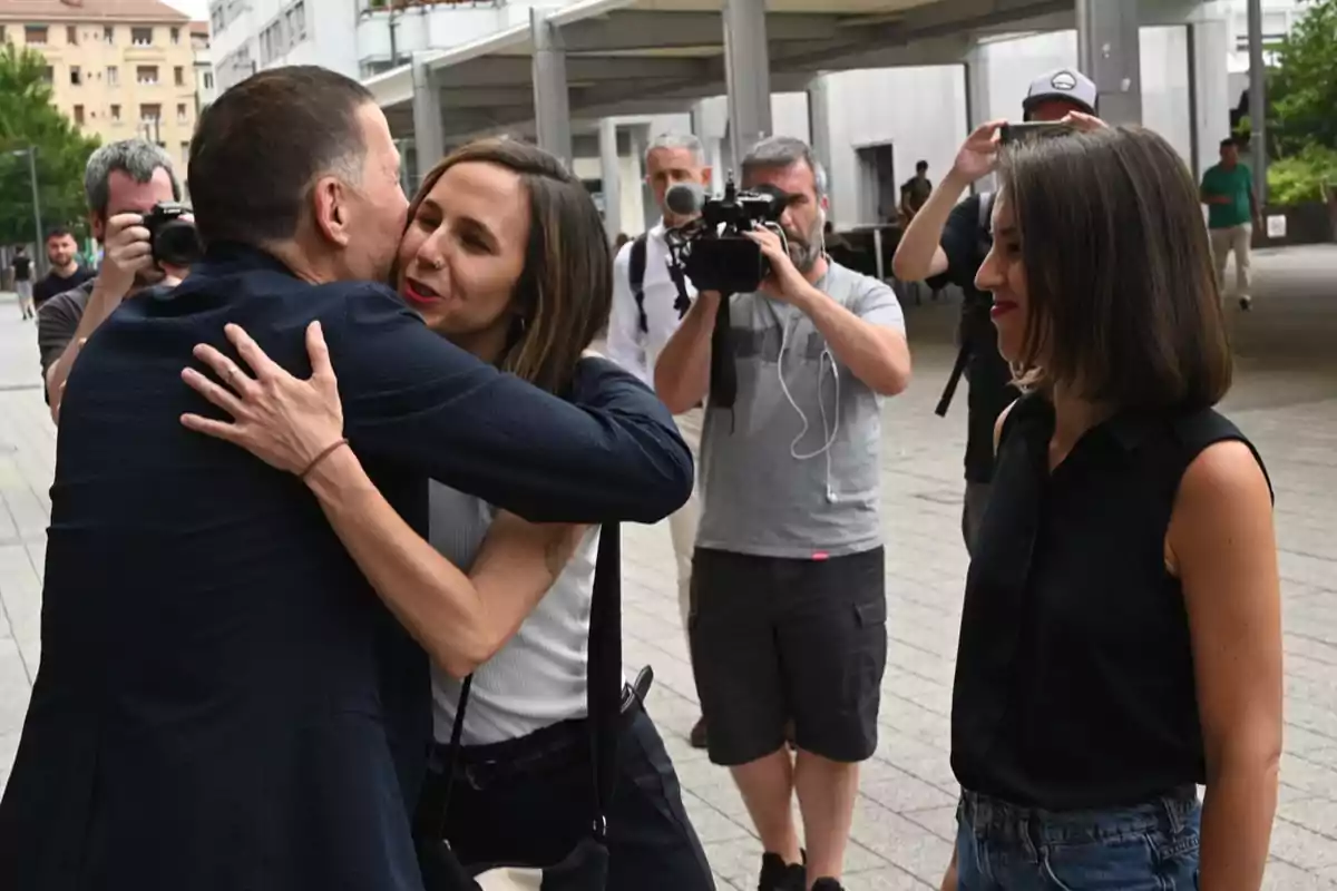 Un hombre y una mujer se abrazan mientras otra mujer observa y varias personas toman fotos y graban en la calle Un hombre y una mujer se abrazan mientras otra mujer observa y varias personas toman fotos y graban en la calle
