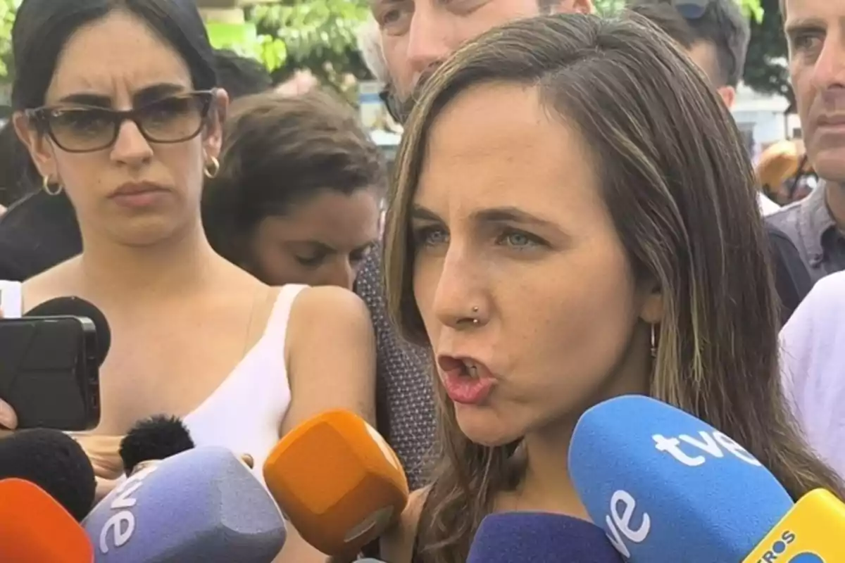 Una mujer hablando frente a varios micrófonos de diferentes medios de comunicación mientras otras personas la rodean