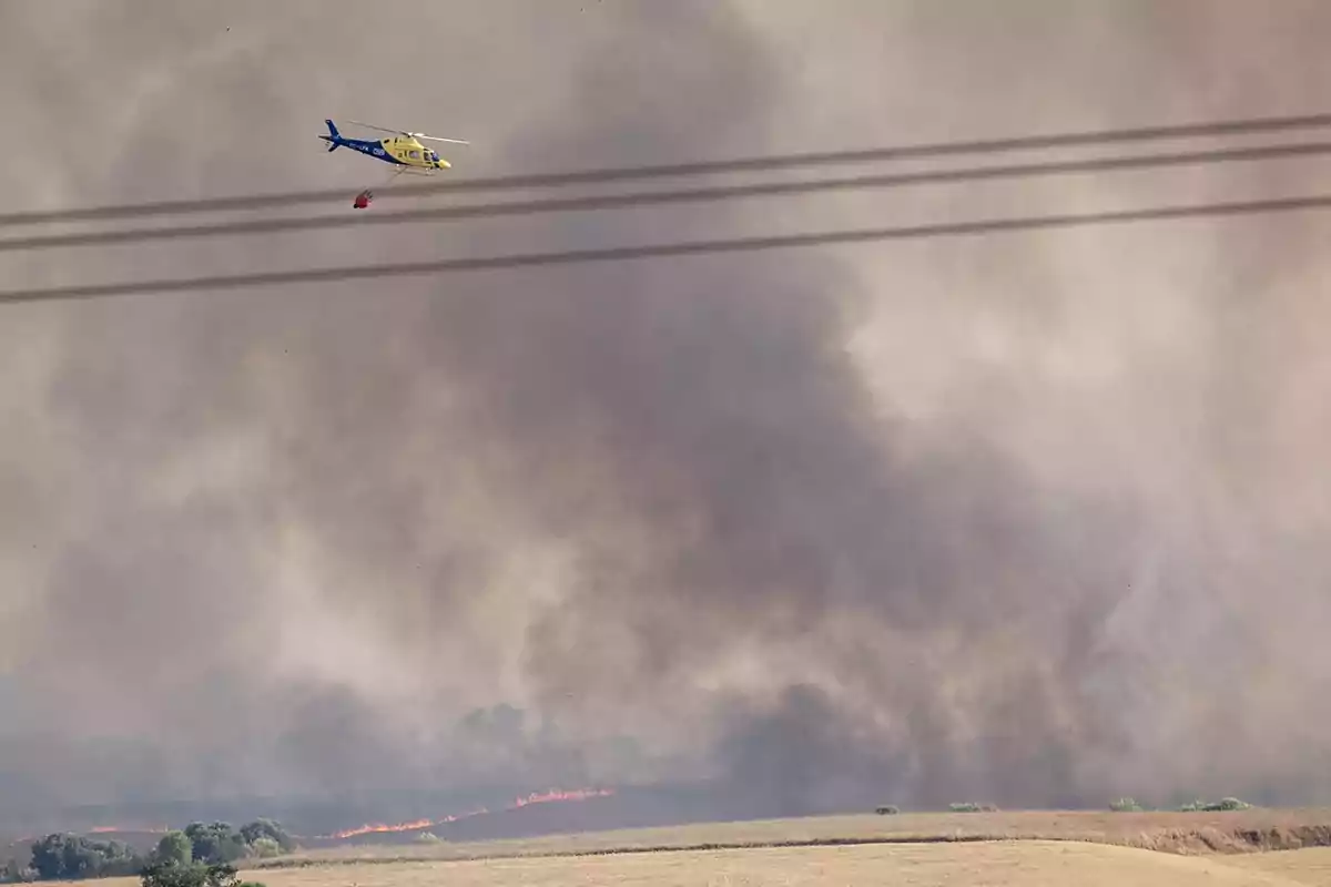 Helicóptero sobrevolando un campo mientras combate un incendio forestal con una gran cantidad de humo en el ambiente
