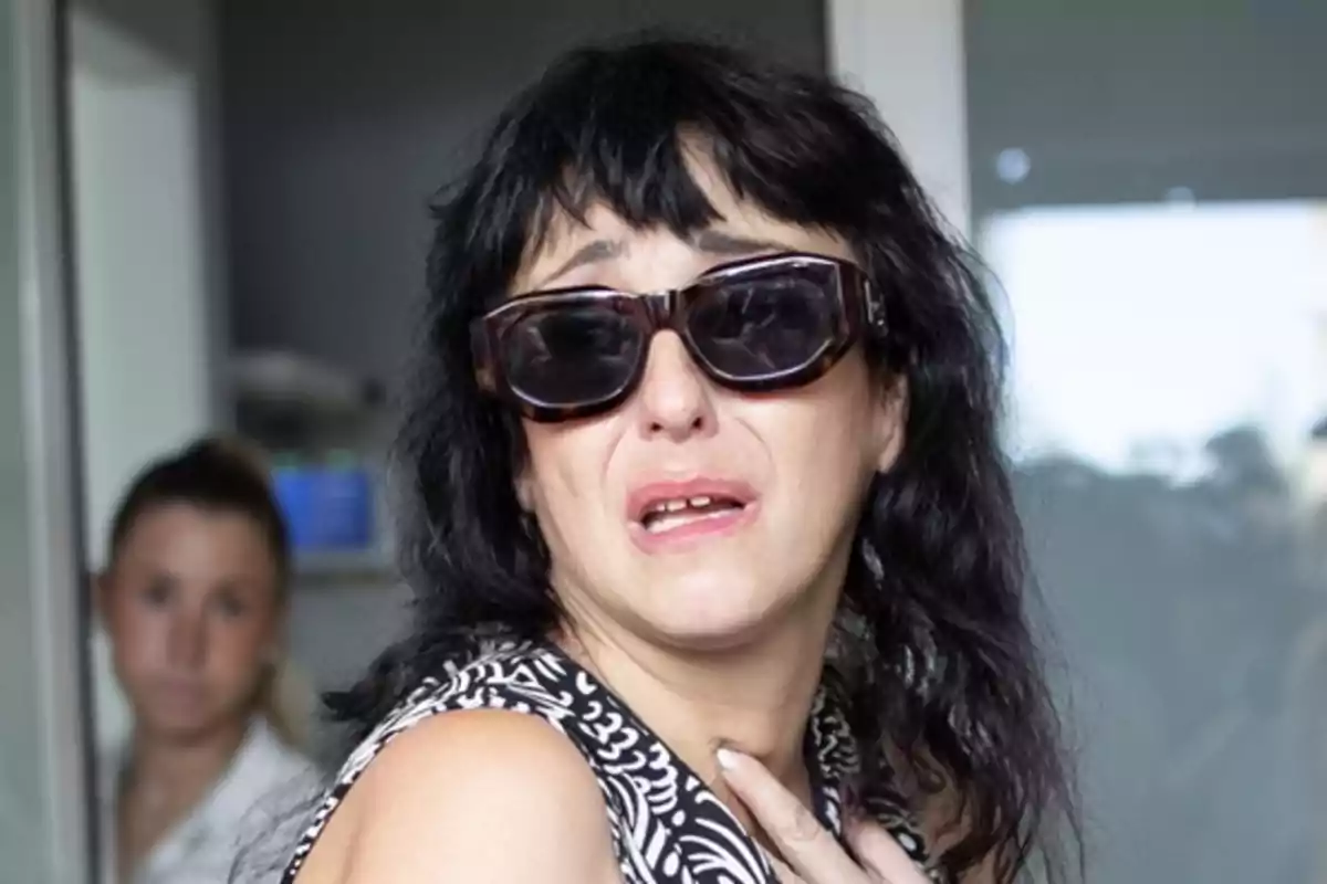 Mujer con gafas oscuras y expresión de angustia en un entorno interior