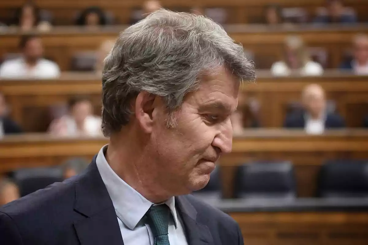 Hombre de cabello canoso con traje y corbata en un recinto parlamentario con personas desenfocadas al fondo Hombre de cabello canoso con traje y corbata en un recinto parlamentario con personas desenfocadas al fondo
