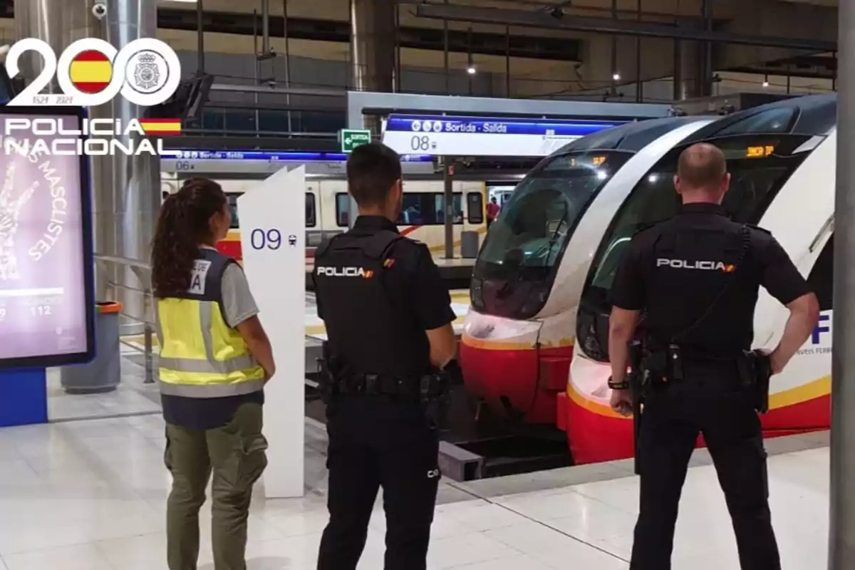 Tres agentes de la policía nacional observan un tren en una estación ferroviaria moderna Tres agentes de la policía nacional observan un tren en una estación ferroviaria moderna