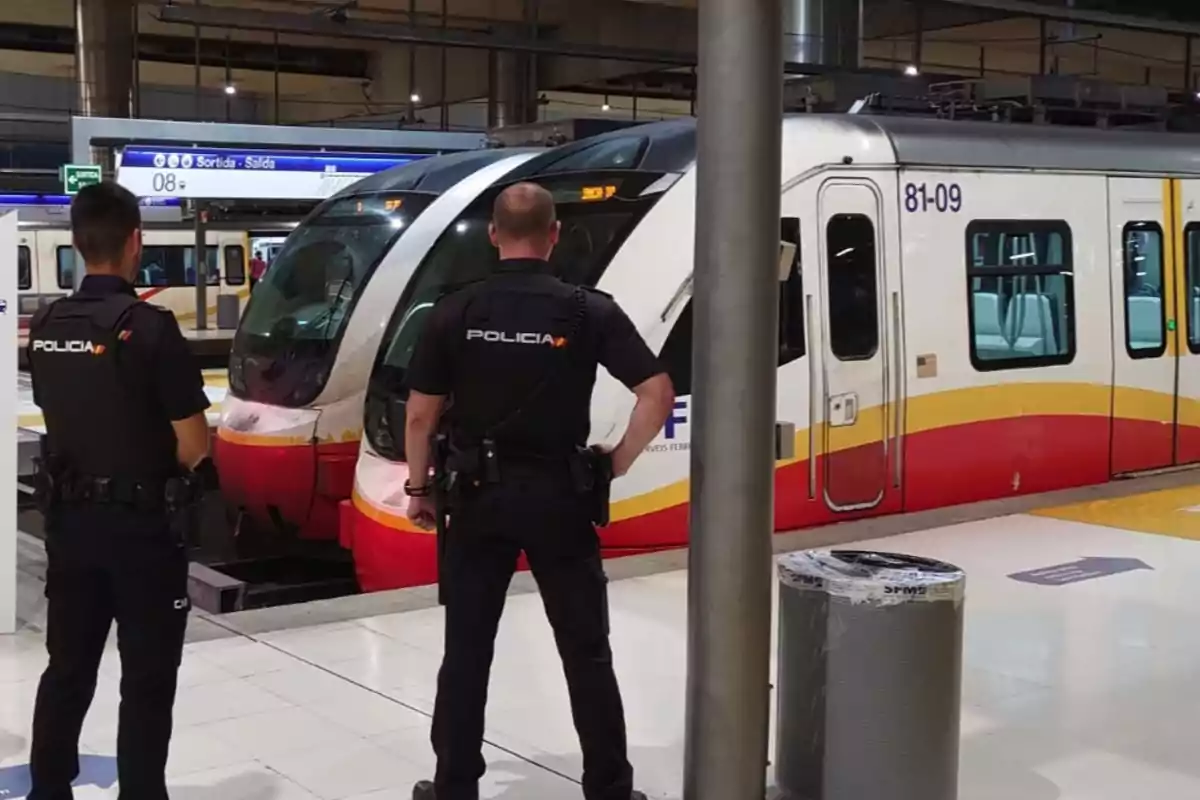 Dos policías de espaldas observan un tren detenido en una estación moderna