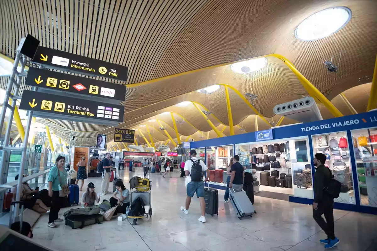 Personas caminando y esperando con maletas en una terminal de aeropuerto moderna con techo de madera y señales de información