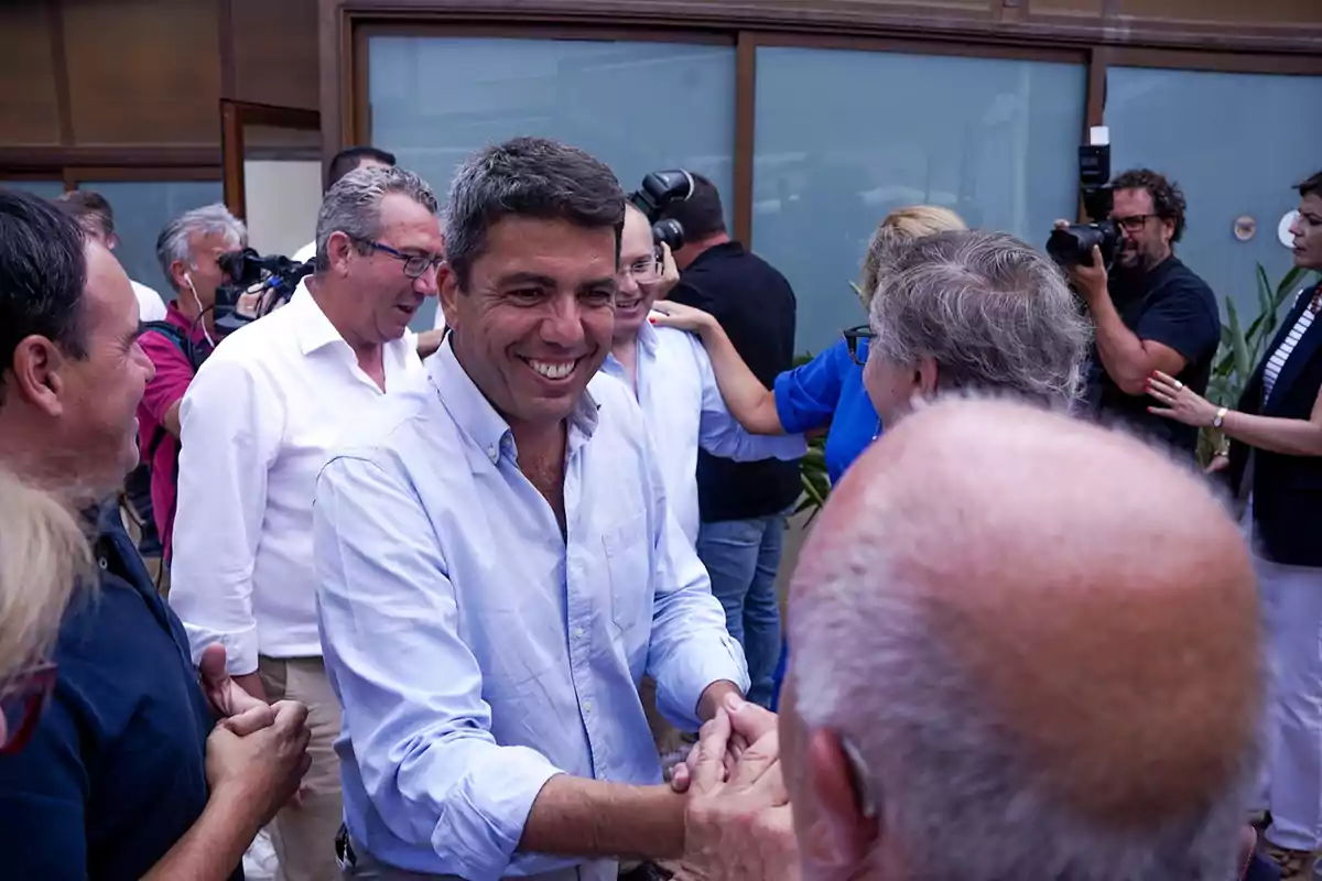 Hombre sonriente saludando a varias personas en un evento social rodeado de cámaras y fotógrafos