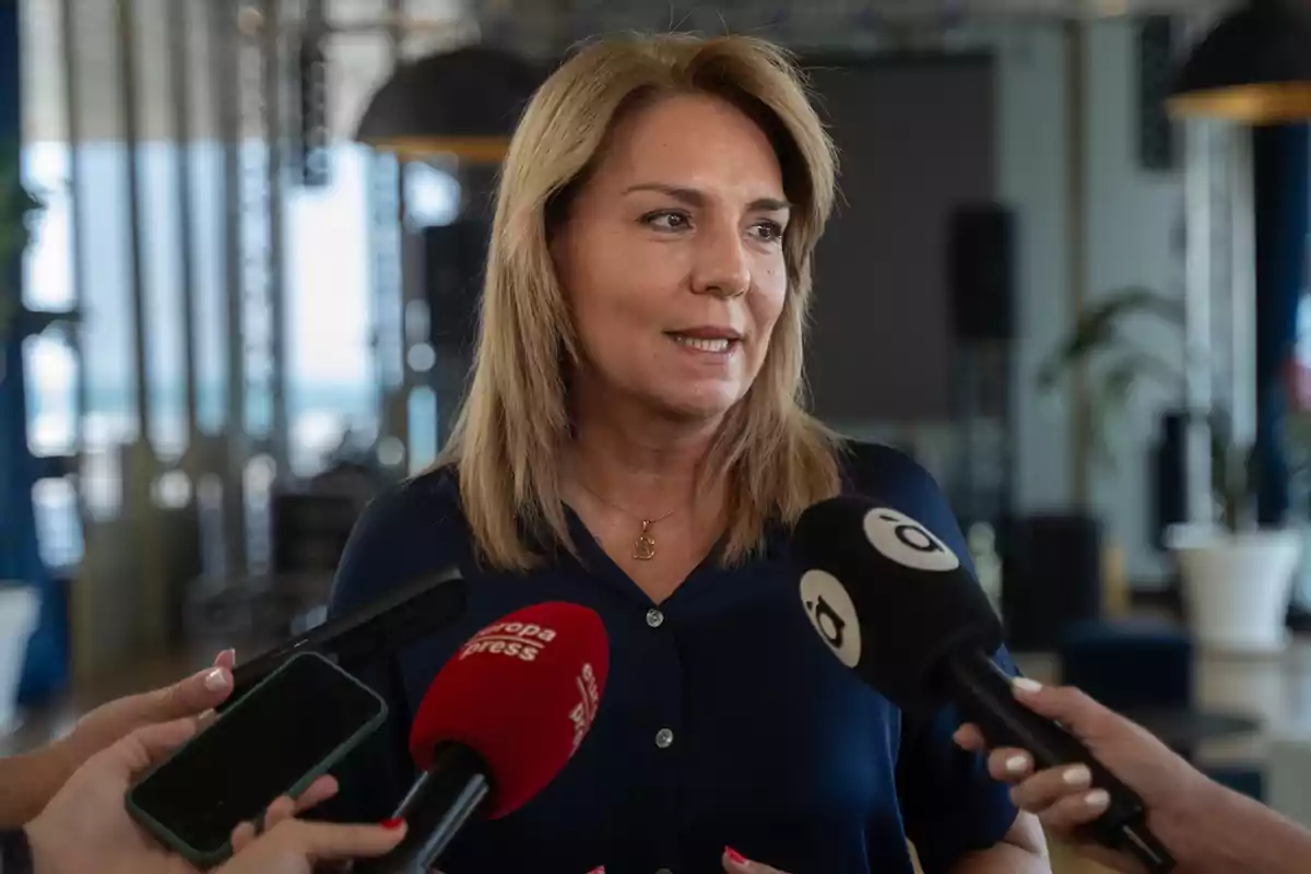 Mujer rubia hablando con varios micrófonos frente a ella en una entrevista dentro de un edificio luminoso Mujer rubia hablando con varios micrófonos frente a ella en una entrevista dentro de un edificio luminoso
