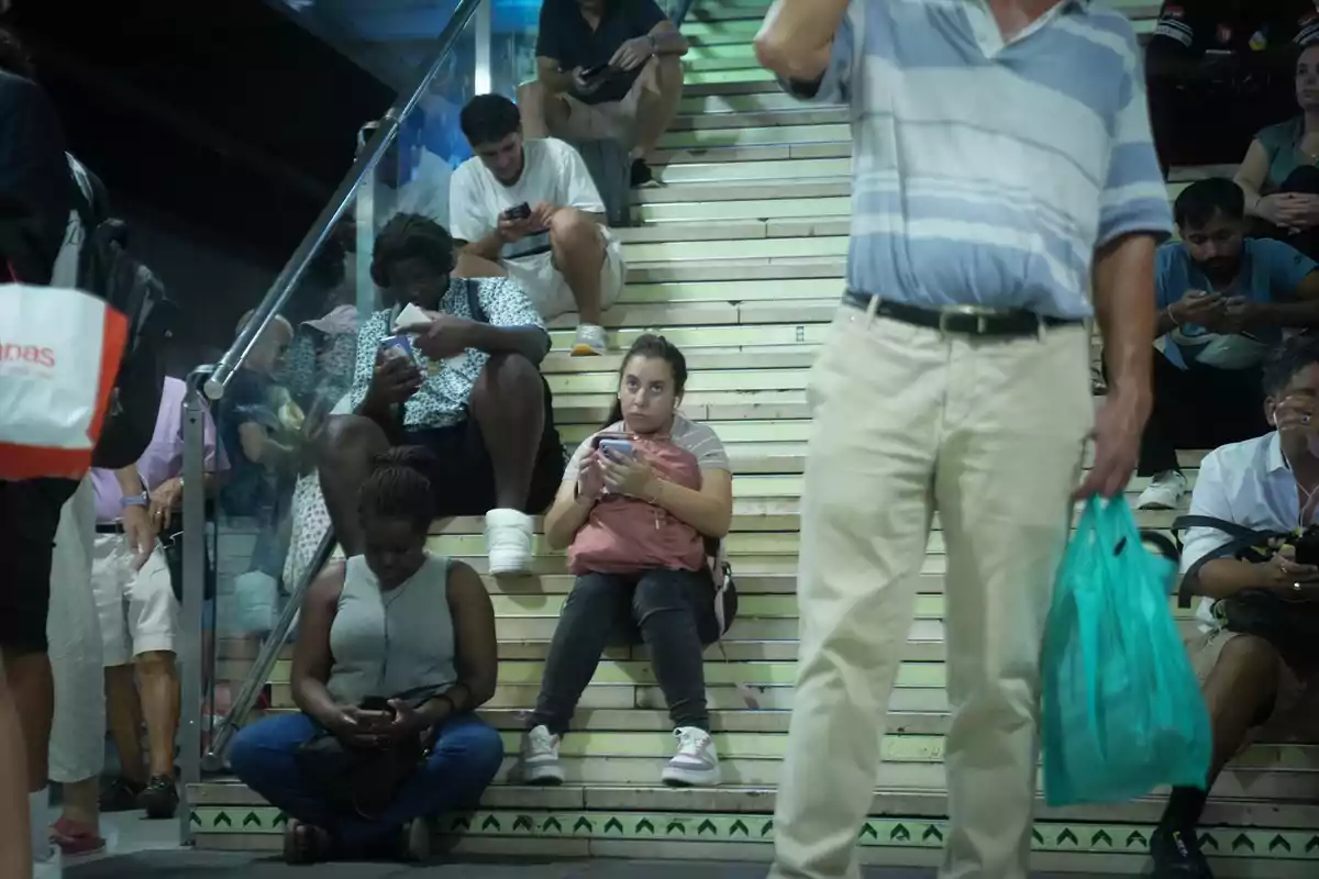 Personas sentadas en unas escaleras usando sus teléfonos móviles en un espacio público concurrido Personas sentadas en unas escaleras usando sus teléfonos móviles en un espacio público concurrido