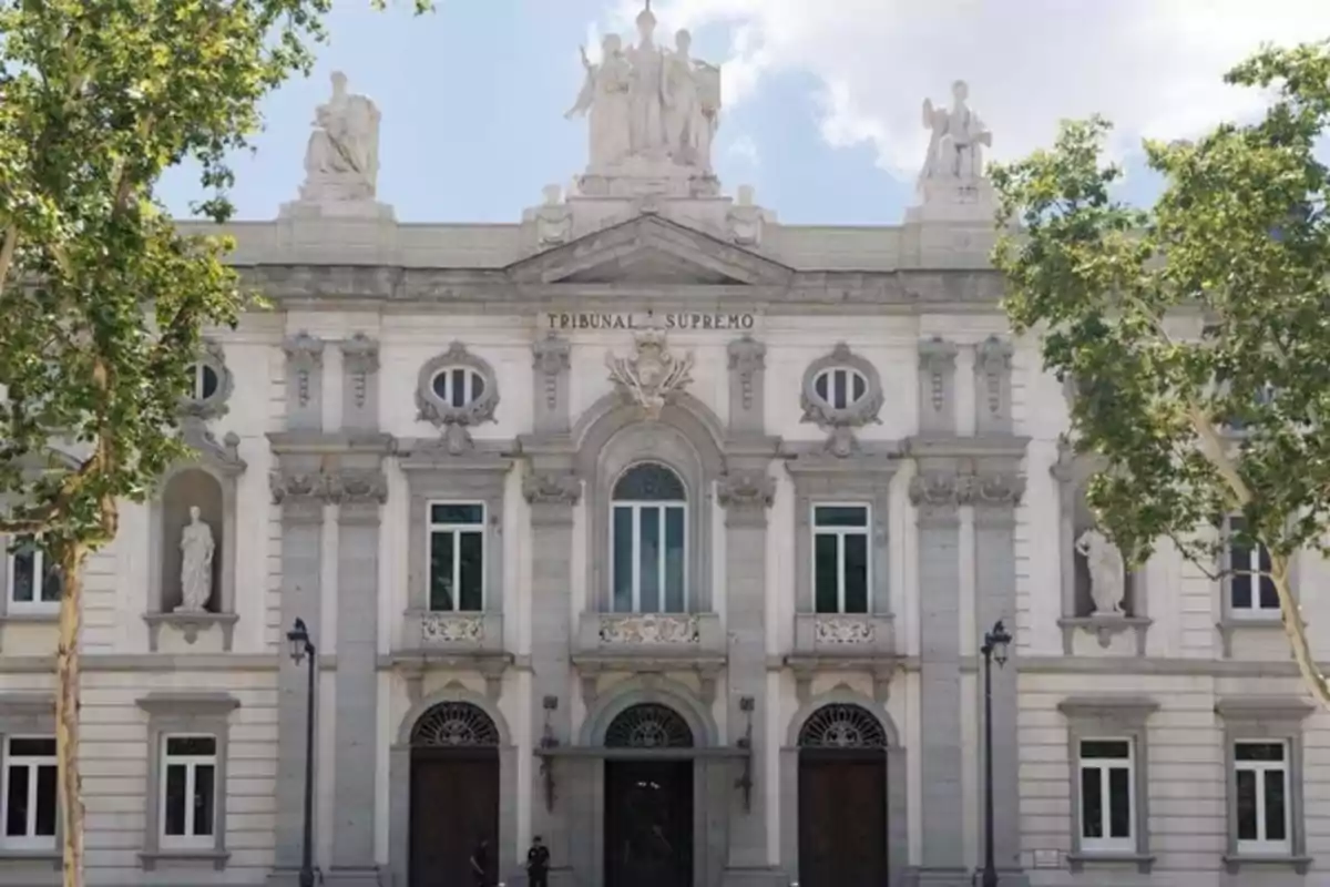 Fachada principal del Tribunal Supremo de España rodeada de árboles y con esculturas en la parte superior del edificio