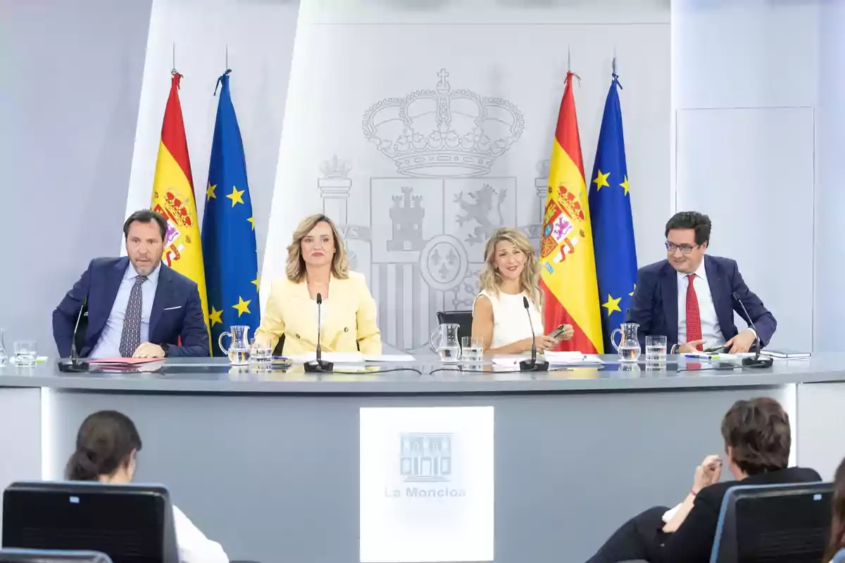 Cuatro personas sentadas en una mesa de conferencia en una sala oficial con banderas de España y la Unión Europea al fondo y el logotipo de La Moncloa en el frente de la mesa Cuatro personas sentadas en una mesa de conferencia en una sala oficial con banderas de España y la Unión Europea al fondo y el logotipo de La Moncloa en el frente de la mesa