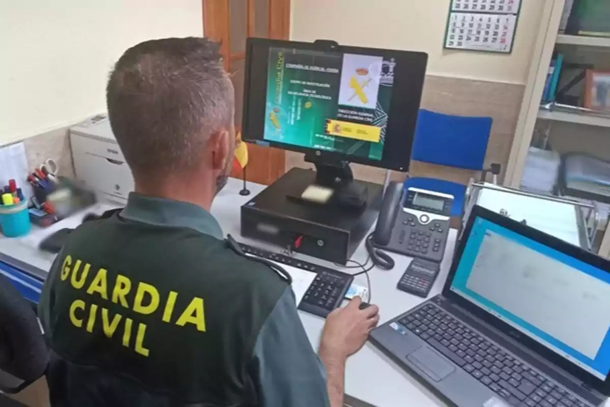 Agente de la Guardia Civil trabajando en una oficina frente a un ordenador con documentos y material de oficina sobre el escritorio Agente de la Guardia Civil trabajando en una oficina frente a un ordenador con documentos y material de oficina sobre el escritorio