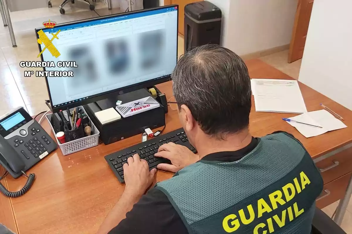 Agente de la Guardia Civil trabajando en una oficina frente a un ordenador con documentos y material de oficina sobre el escritorio