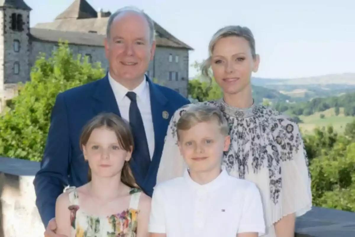 A family of four—Alberto of Monaco, Charlene, and their two children—pose outdoors in front of a castle and a green landscape.