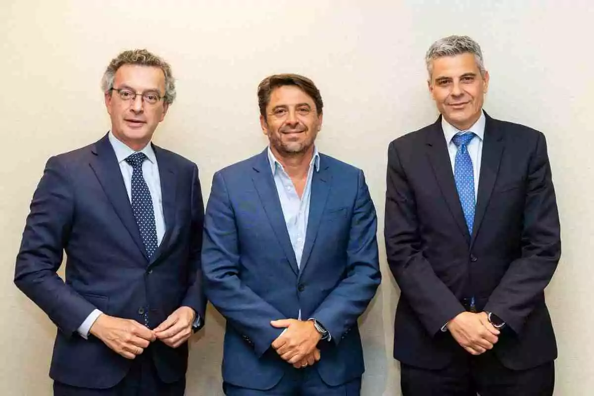 Tres hombres vestidos con traje posan juntos frente a una pared clara Tres hombres vestidos con traje posan juntos frente a una pared clara
