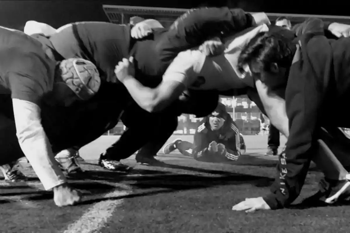 Jugadores de rugby realizando una melé durante un entrenamiento nocturno mientras una persona observa desde el suelo al fondo