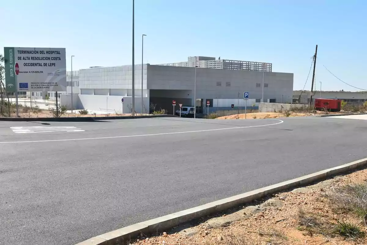 Edificio moderno de hospital en una zona despejada con un cartel informativo y una carretera asfaltada en primer plano Edificio moderno de hospital en una zona despejada con un cartel informativo y una carretera asfaltada en primer plano