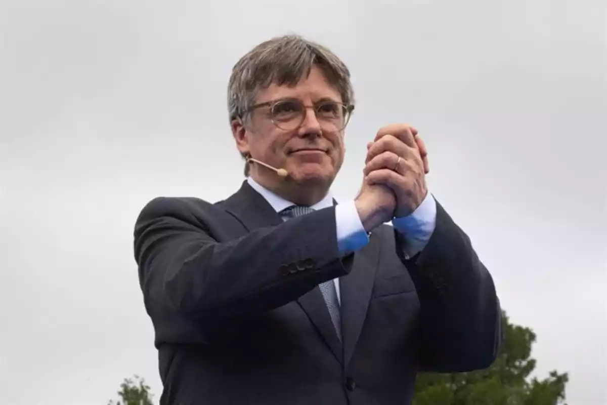 Hombre con gafas y micrófono de diadema vestido con traje oscuro aplaudiendo al aire libre bajo un cielo nublado Hombre con gafas y micrófono de diadema vestido con traje oscuro aplaudiendo al aire libre bajo un cielo nublado
