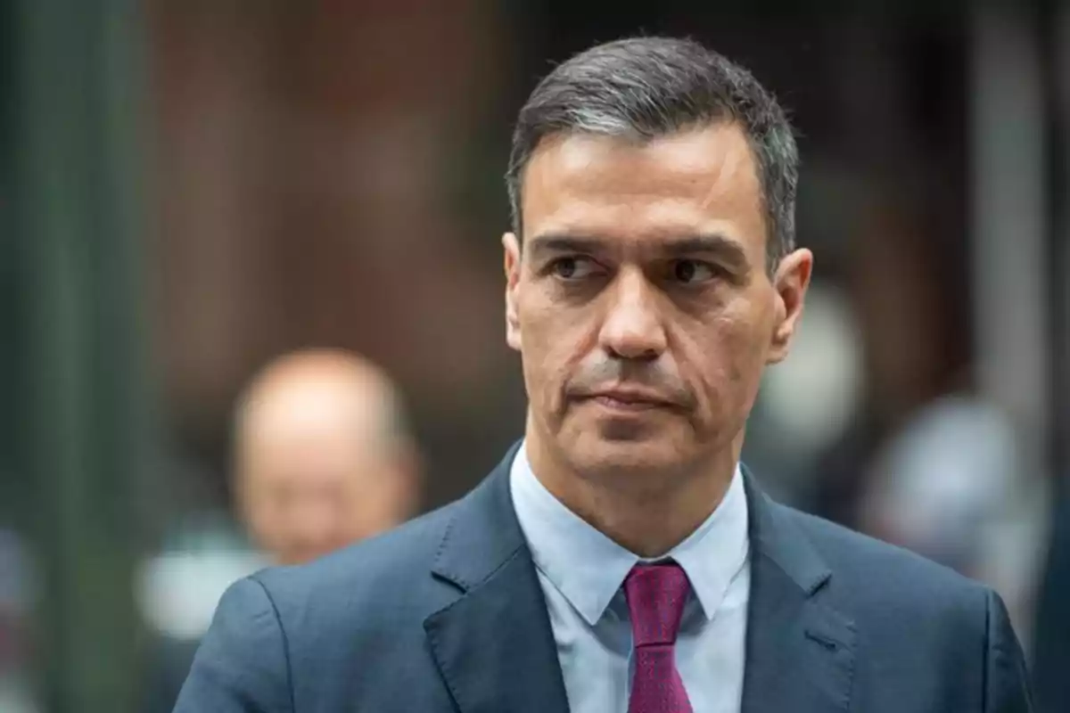 Hombre de cabello corto y canoso con traje azul y corbata roja mirando hacia un lado en un entorno urbano desenfocado Hombre de cabello corto y canoso con traje azul y corbata roja mirando hacia un lado en un entorno urbano desenfocado