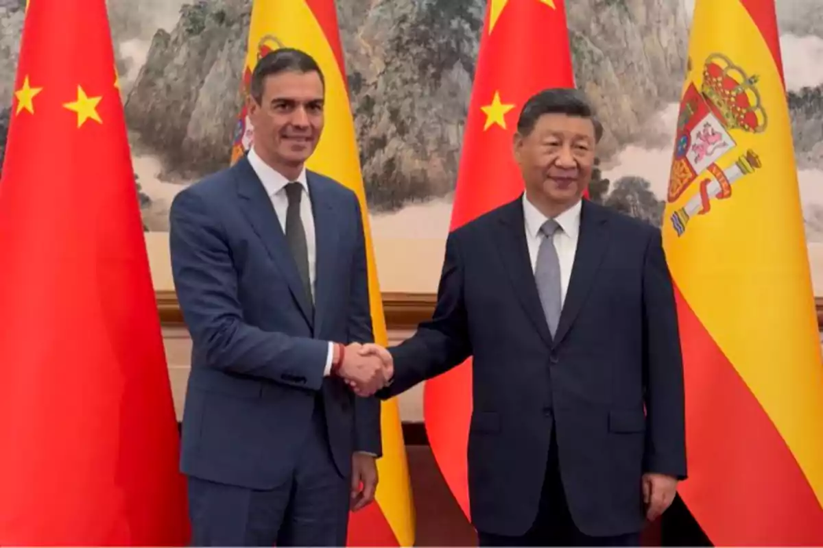 Dos hombres con traje se dan la mano frente a banderas de China y España Dos hombres con traje se dan la mano frente a banderas de China y España