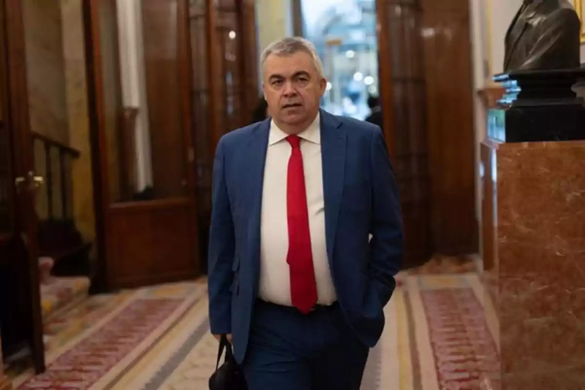 Hombre de cabello canoso con traje azul y corbata roja caminando por un pasillo elegante con alfombra y paredes de madera Hombre de cabello canoso con traje azul y corbata roja caminando por un pasillo elegante con alfombra y paredes de madera