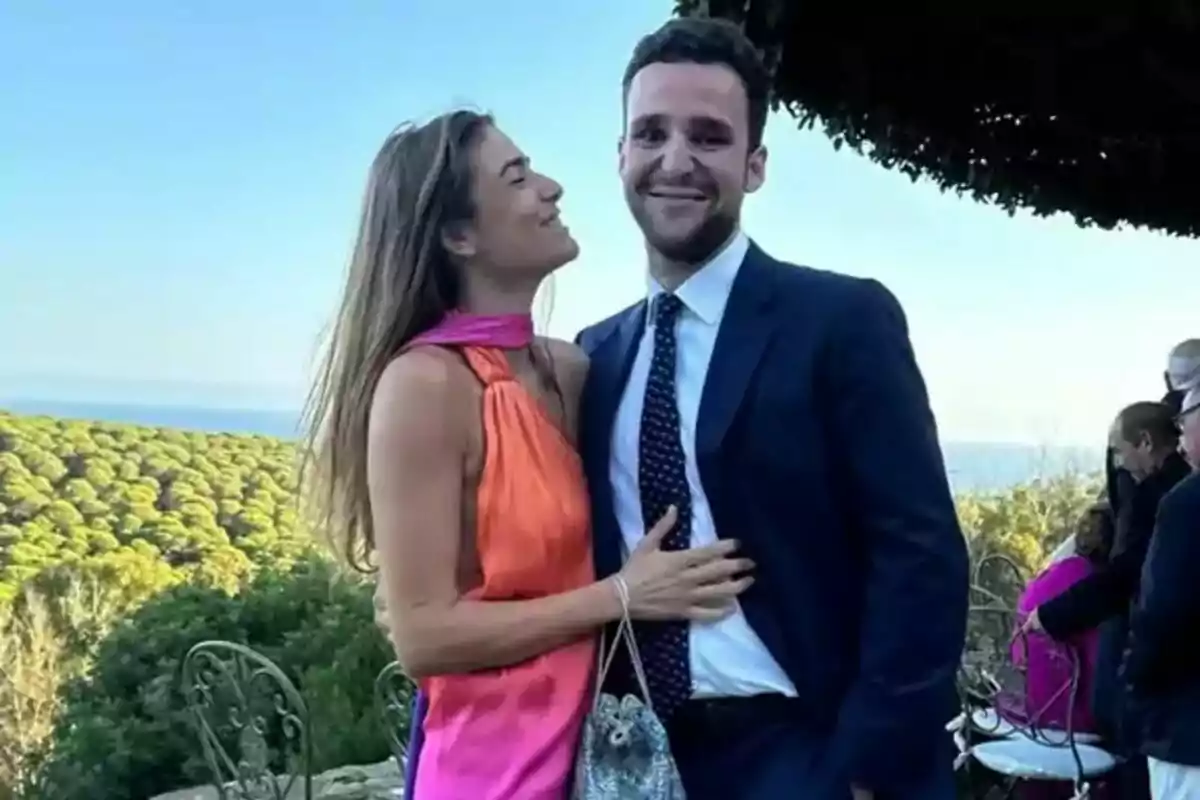 Smiling couple posing outdoors, Froilán and Candela Martínez Aralejo, with a background of trees and the sea at an elegant event. Smiling couple posing outdoors, Froilán and Candela Martínez Aralejo, with a background of trees and the sea at an elegant event.