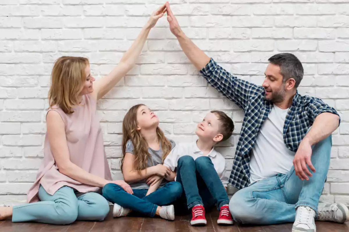Familia sentada en el suelo sonriendo y tocando sus manos formando un techo mientras dos niños los observan
