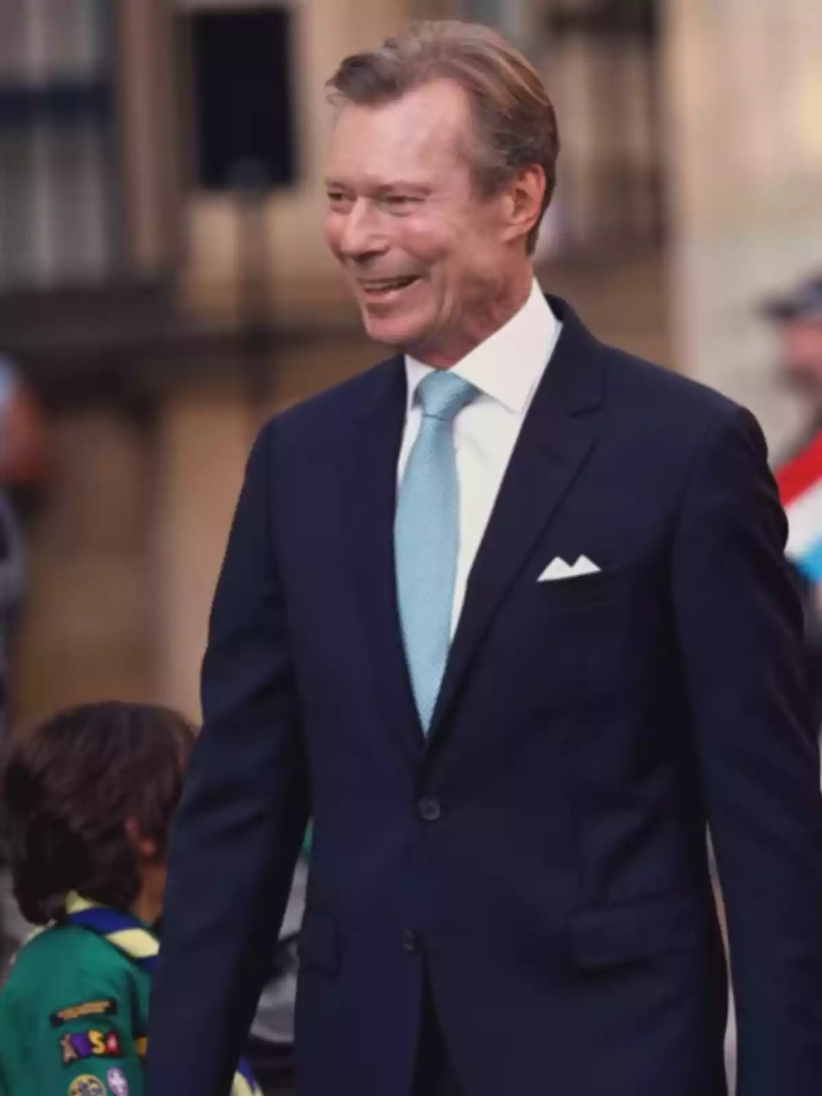 Middle-aged man in a blue suit and light blue tie smiling at an outdoor event Middle-aged man in a blue suit and light blue tie smiling at an outdoor event