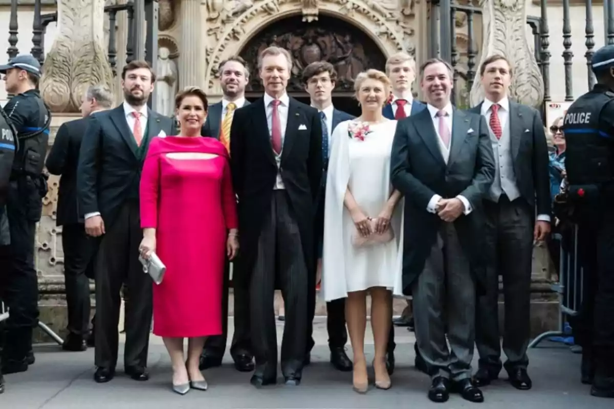 A group of elegantly dressed people poses in front of a historic building with decorative architectural details and police officers on either side. A group of elegantly dressed people poses in front of a historic building with decorative architectural details and police officers on either side.