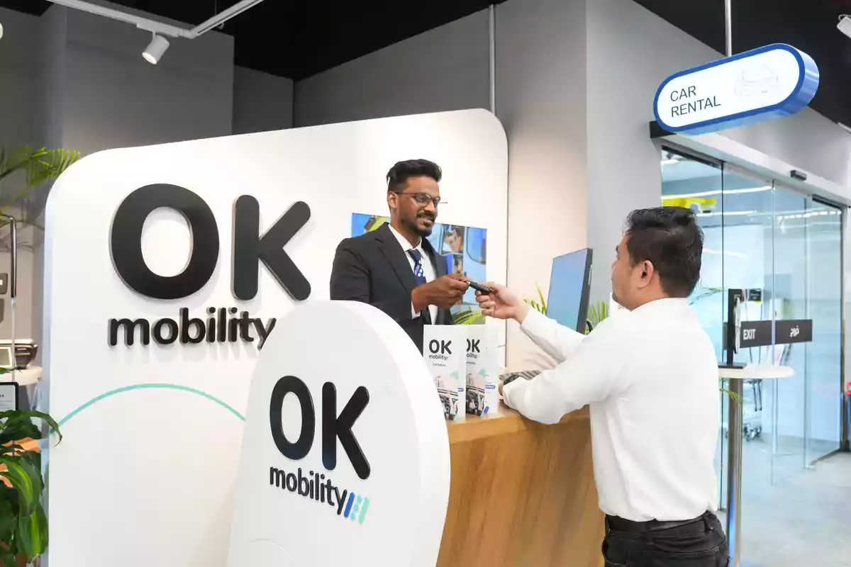Empleado de OK Mobility entregando las llaves de un coche a un cliente en el mostrador de alquiler de autos