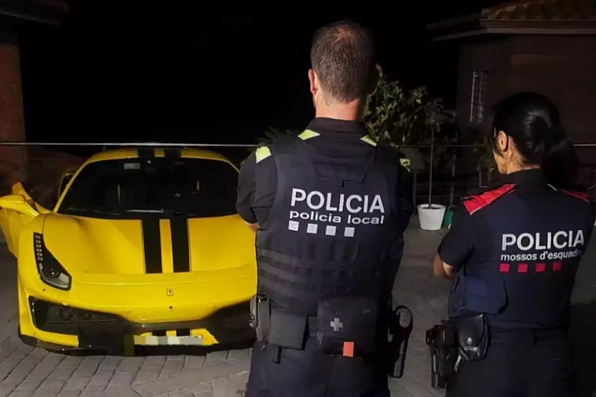 Dos agentes de policía de espaldas observan un coche deportivo amarillo estacionado en una calle por la noche