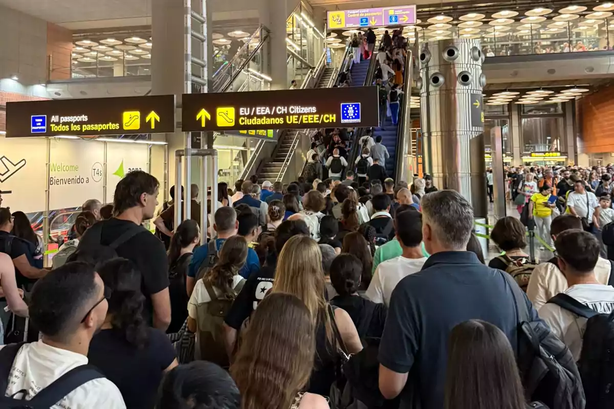 Gran cantidad de personas haciendo fila en un aeropuerto para pasar por el control de pasaportes, con letreros que indican diferentes filas para ciudadanos de la Unión Europea y para todos los pasaportes. Gran cantidad de personas haciendo fila en un aeropuerto para pasar por el control de pasaportes, con letreros que indican diferentes filas para ciudadanos de la Unión Europea y para todos los pasaportes.