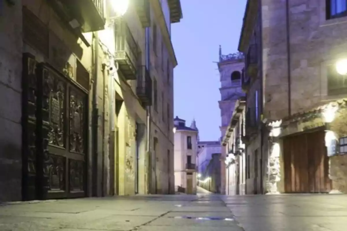 Callejón empedrado y vacío al atardecer con edificios antiguos y faroles encendidos Callejón empedrado y vacío al atardecer con edificios antiguos y faroles encendidos