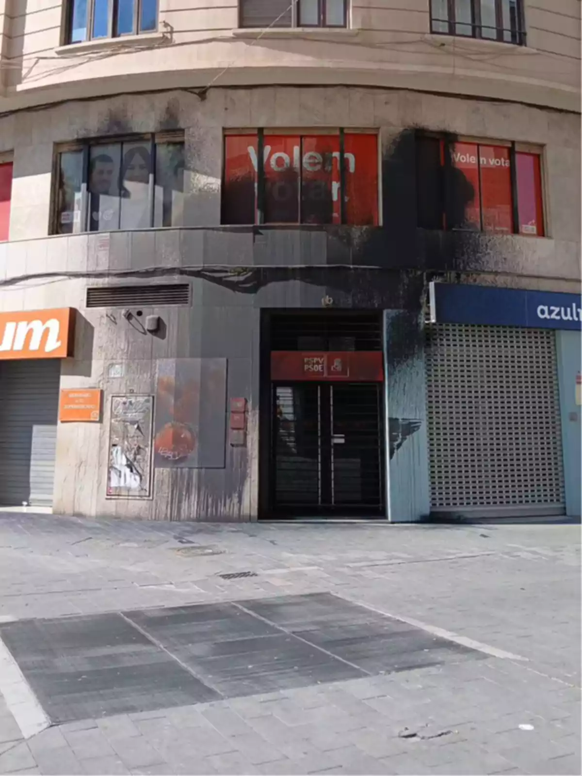 Fachada de edificio con ventanas y puerta manchadas de negro, probablemente por un incendio o acto vandálico, en una calle urbana Fachada de edificio con ventanas y puerta manchadas de negro, probablemente por un incendio o acto vandálico, en una calle urbana