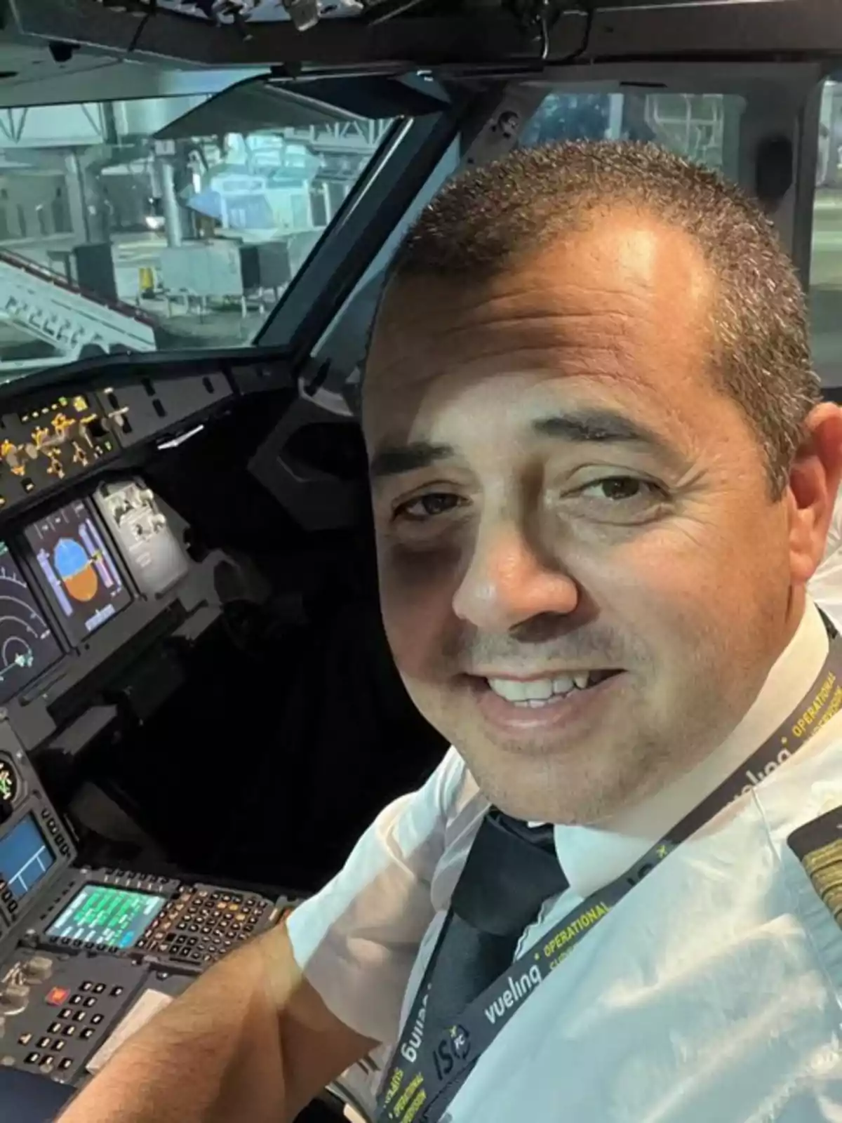 Piloto sonriente sentado en la cabina de un avión con controles y pantallas encendidos al fondo Piloto sonriente sentado en la cabina de un avión con controles y pantallas encendidos al fondo