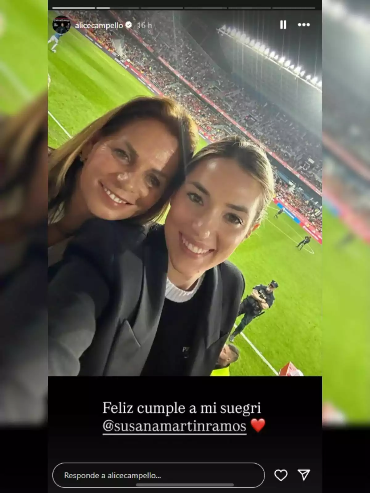 Dos mujeres sonríen -que son Alice Campello y su suegra- y se toman una selfie en un estadio de fútbol lleno de espectadores, con el campo iluminado de fondo y un mensaje de felicitación en la parte inferior de la imagen. Dos mujeres sonríen -que son Alice Campello y su suegra- y se toman una selfie en un estadio de fútbol lleno de espectadores, con el campo iluminado de fondo y un mensaje de felicitación en la parte inferior de la imagen.