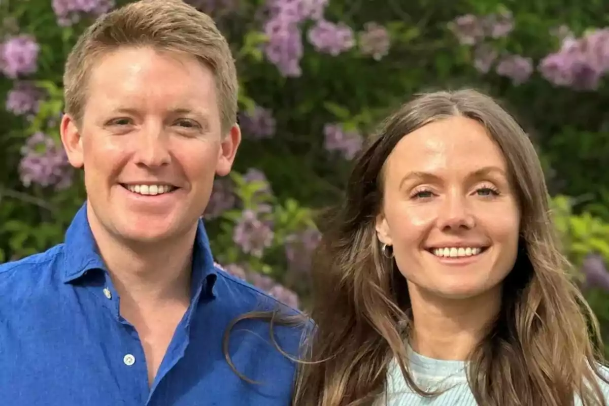 A smiling couple poses outdoors with lilac flowers in the background. A smiling couple poses outdoors with lilac flowers in the background.
