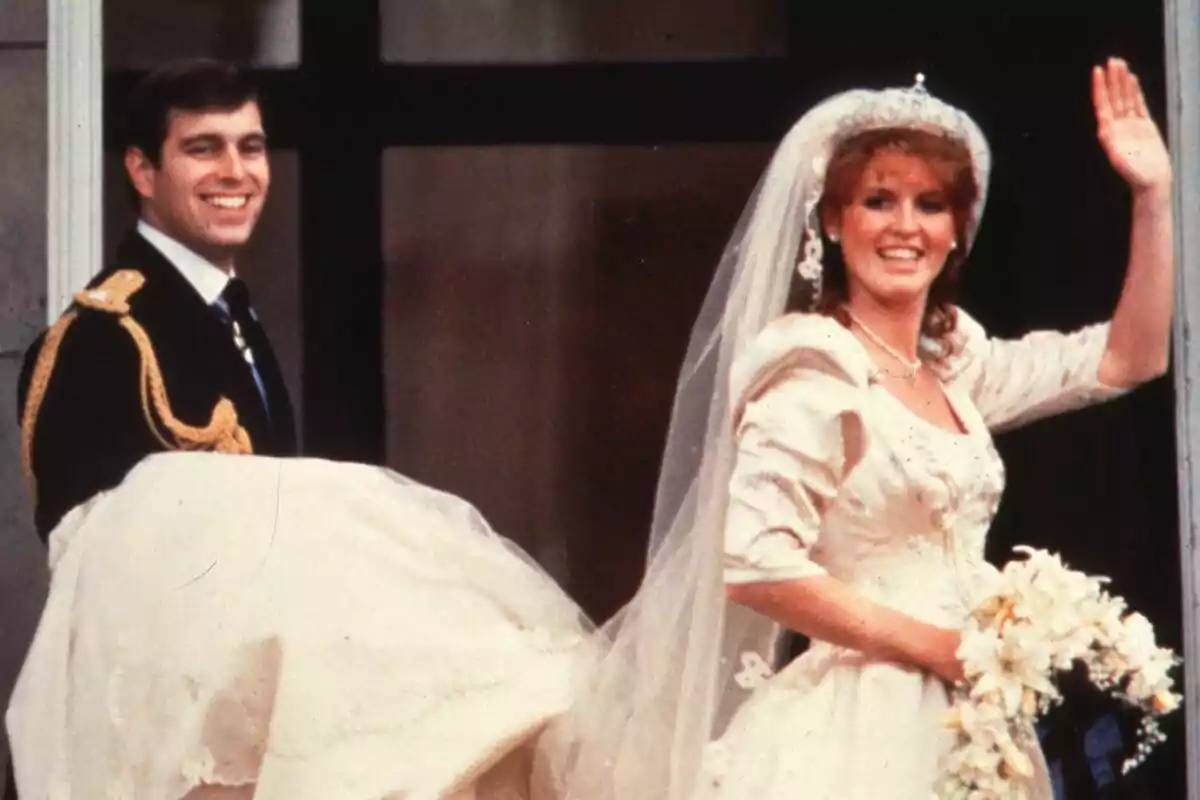 Pareja sonriente en su boda, la novia lleva un vestido blanco con velo y ramo de flores, el novio viste uniforme oscuro con detalles dorados Pareja sonriente en su boda, la novia lleva un vestido blanco con velo y ramo de flores, el novio viste uniforme oscuro con detalles dorados