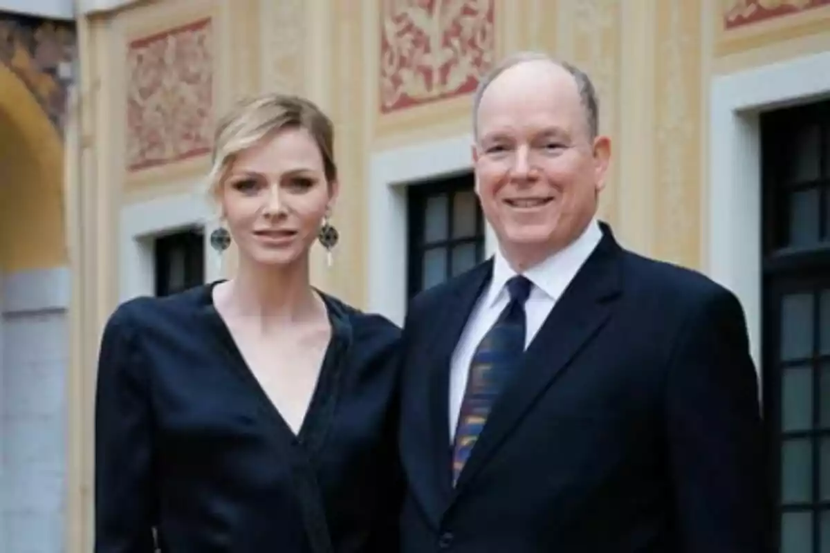 Elegantly dressed couple, Alberto and Charlene of Monaco, posing in front of a building with decorative architectural details. Elegantly dressed couple, Alberto and Charlene of Monaco, posing in front of a building with decorative architectural details.