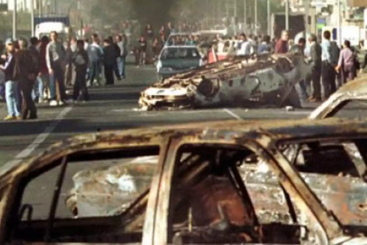 Personas observan una calle bloqueada por autos quemados y volcados