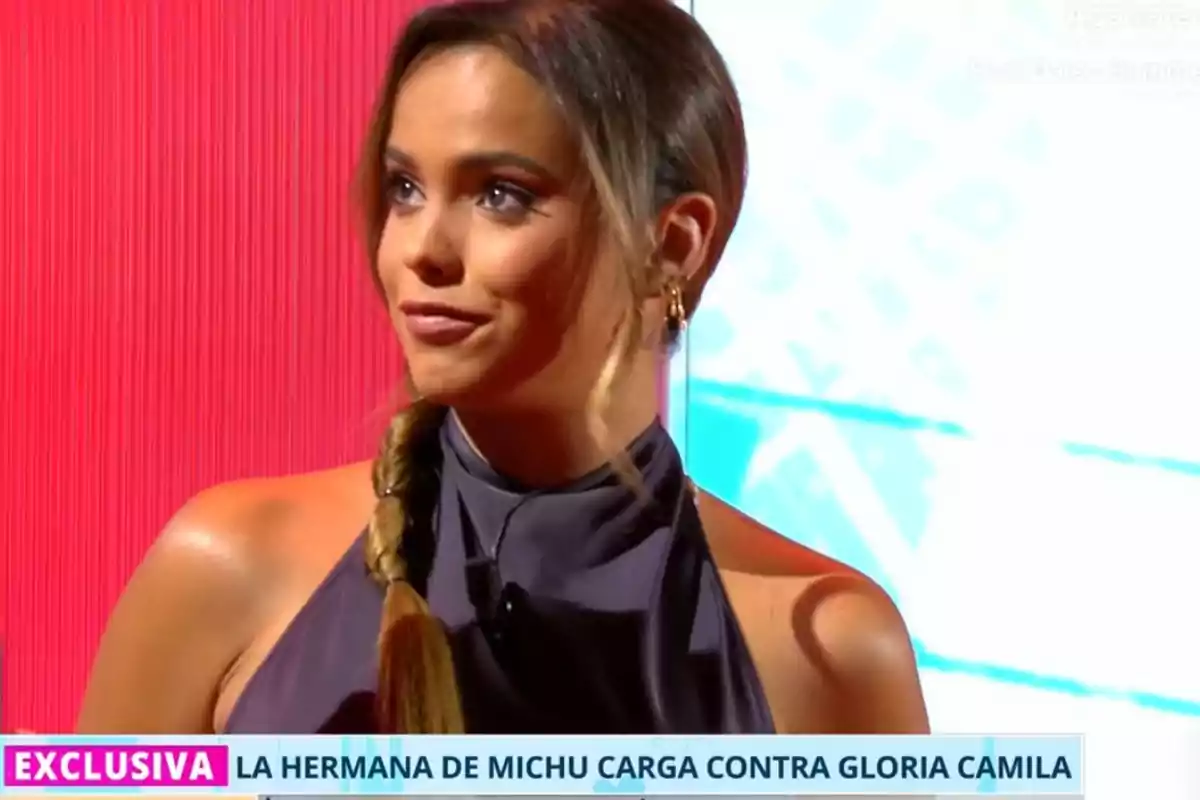 Gloria Camila joven con coleta y vestido gris en un plató de televisión con fondo rojo y azul, aparece un rótulo informativo en la parte inferior Gloria Camila joven con coleta y vestido gris en un plató de televisión con fondo rojo y azul, aparece un rótulo informativo en la parte inferior