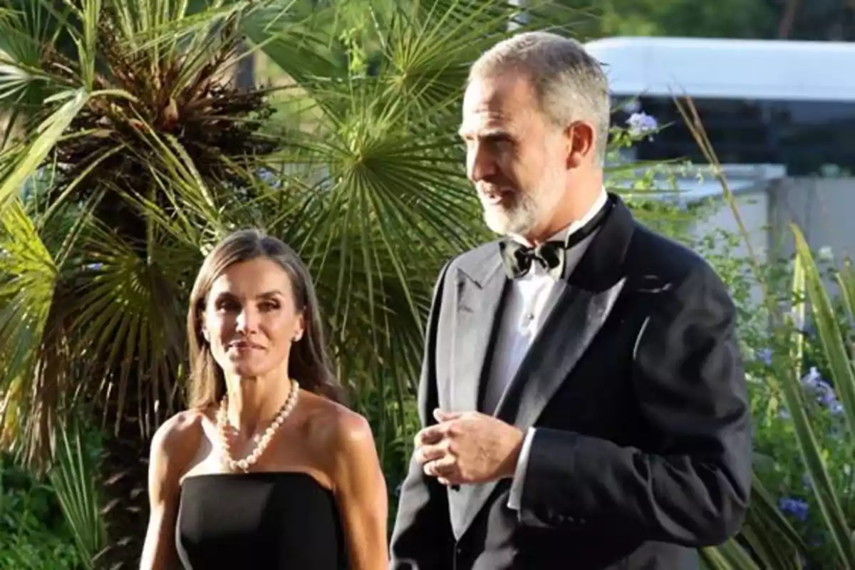 An elegantly dressed couple walks outdoors among palm trees and greenery. An elegantly dressed couple walks outdoors among palm trees and greenery.