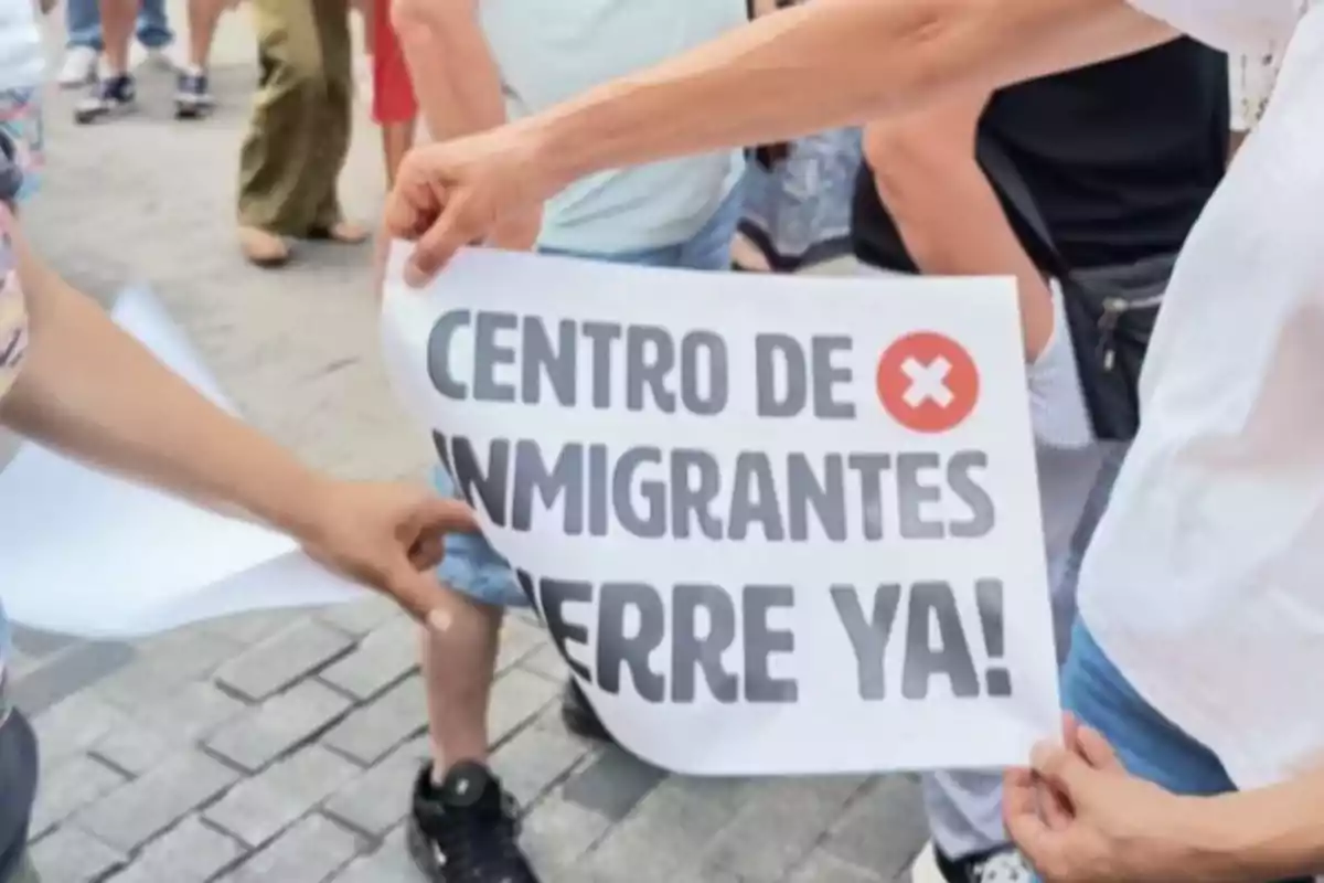 Personas sostienen un cartel en una manifestación que pide el cierre de un centro de inmigrantes.