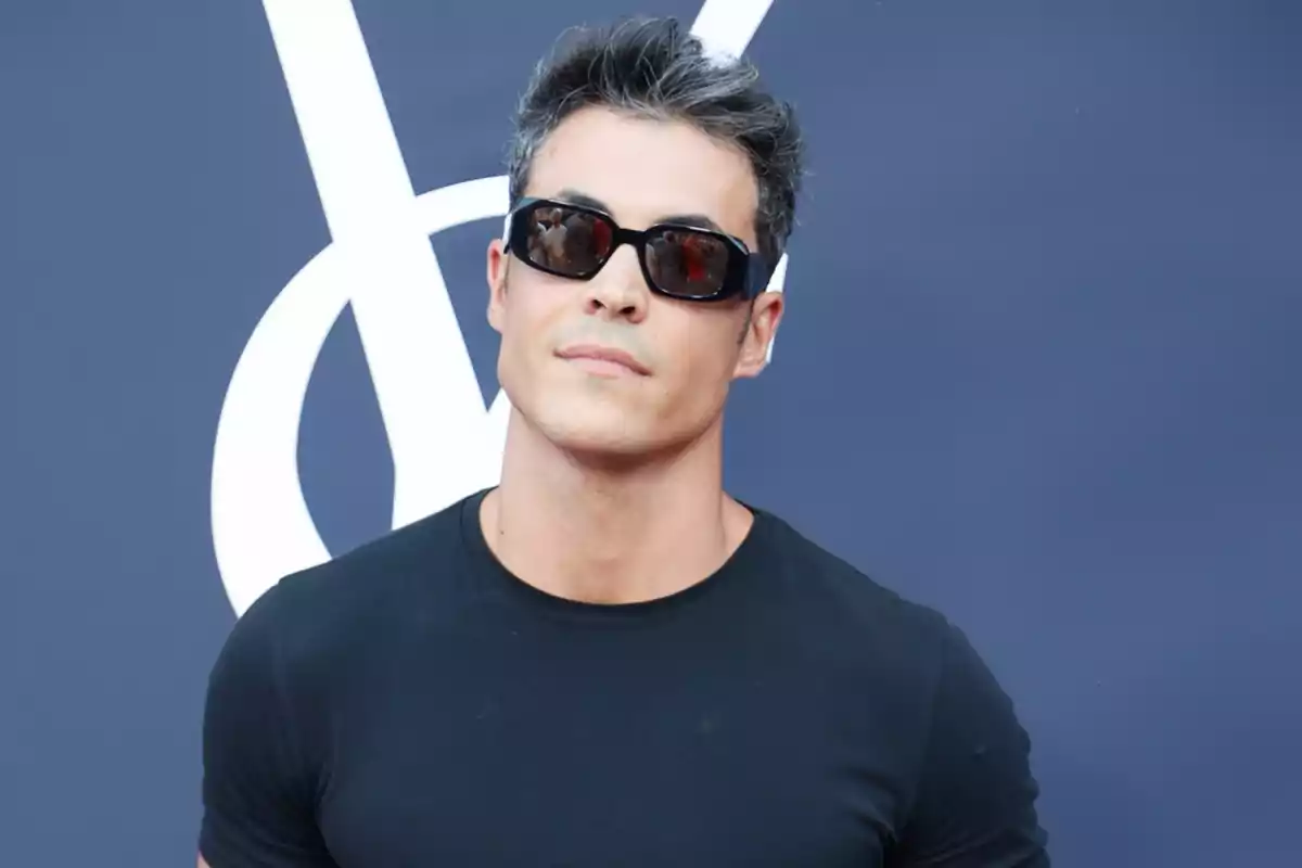 Kiko Jiménez usando gafas de sol y camiseta negra posando frente a un fondo azul Kiko Jiménez usando gafas de sol y camiseta negra posando frente a un fondo azul