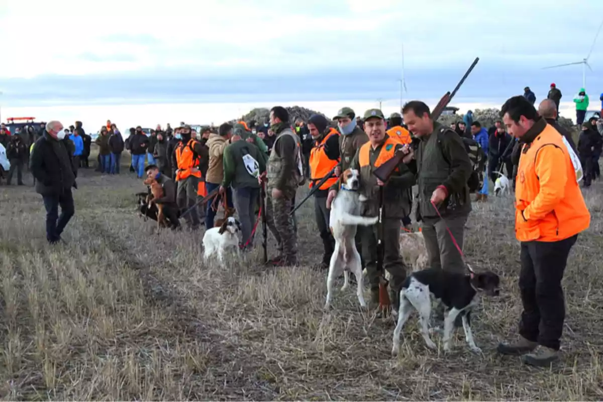 Grupo de personas con chalecos naranjas y perros en un campo durante una jornada de caza