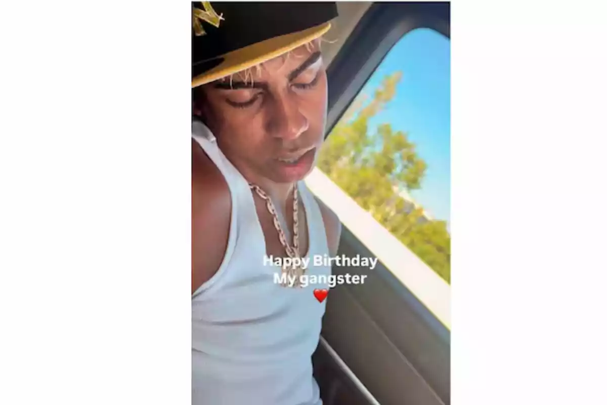 Joven con gorra negra y camiseta blanca sentado junto a una ventana en un auto con la frase Happy Birthday My gangster y un emoji de corazón rojo Joven con gorra negra y camiseta blanca sentado junto a una ventana en un auto con la frase Happy Birthday My gangster y un emoji de corazón rojo
