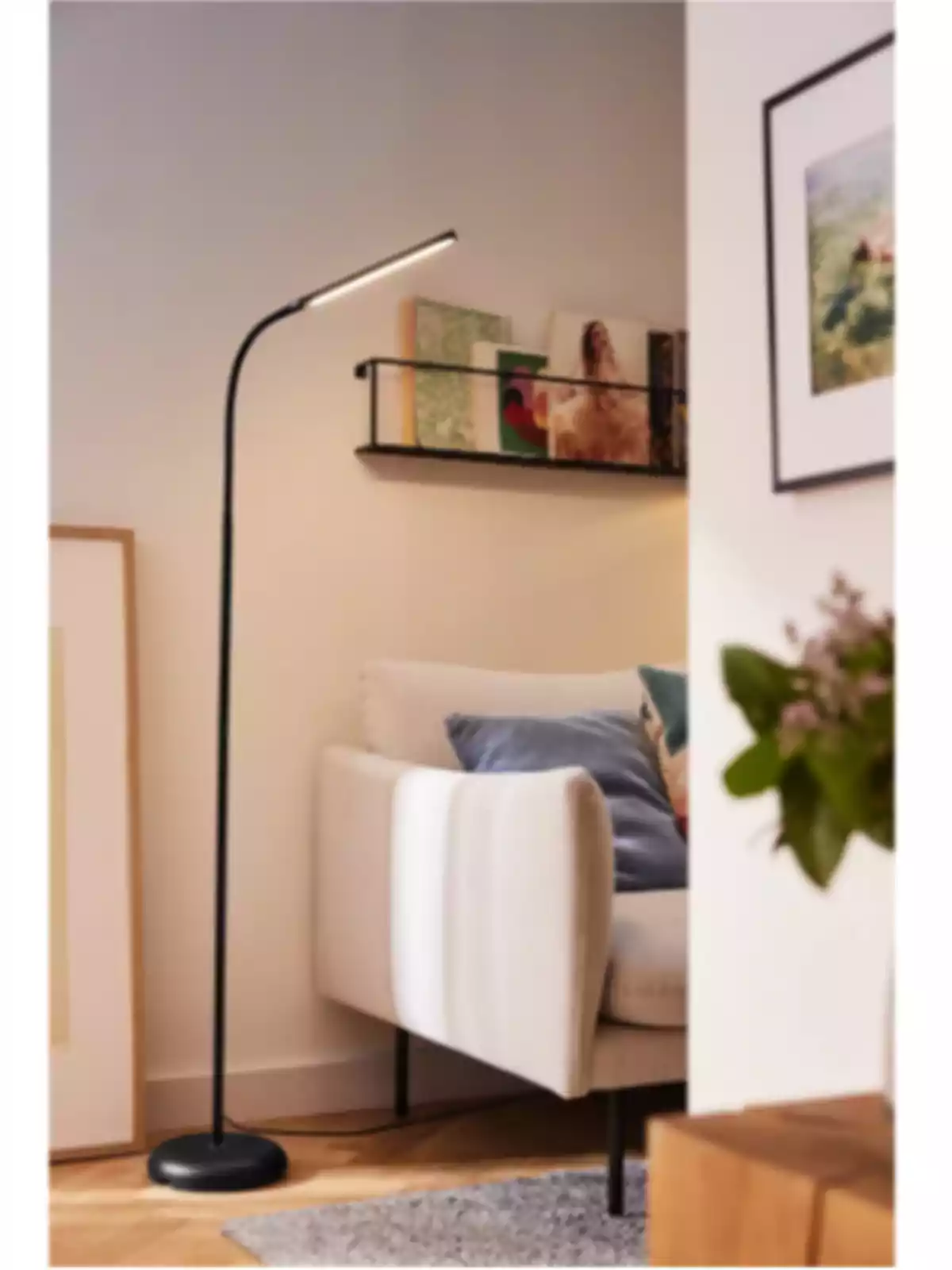 Lámpara de pie negra junto a un sofá beige con cojines en una sala decorada con cuadros y estantería de libros Lámpara de pie negra junto a un sofá beige con cojines en una sala decorada con cuadros y estantería de libros