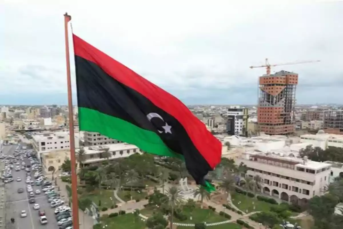 Bandera de Libia ondeando sobre una ciudad con edificios modernos y áreas verdes Bandera de Libia ondeando sobre una ciudad con edificios modernos y áreas verdes
